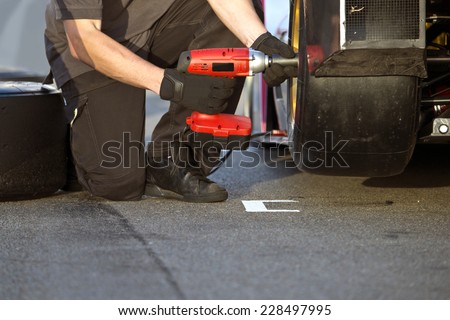 Race car being serviced with new slick tires by a mechanic during a race in the pit lane
