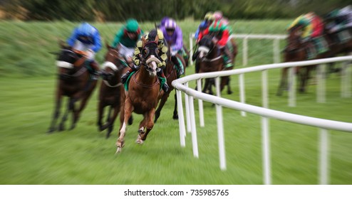 Race Horses And Jockeys Racing Fast Around The Turn Of The Track With Motion Blur Effect 