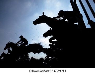 race horses jumping over a hurdle at speed photographed in silhouette
