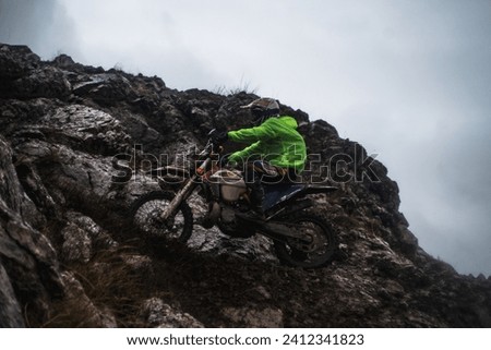 A racer at a competition rides along a cliff in rainy and gloomy weather, bottom view, professional motorcyclist in full moto equipment riding crops enduro bike in highlands Stock photo © 