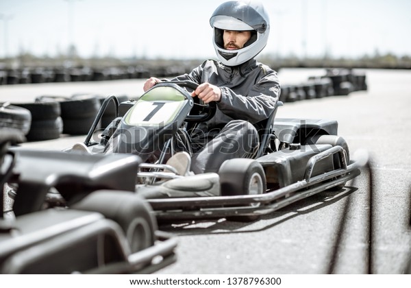 Racer in sportswear and protective helmet driving\
go-kart on the track