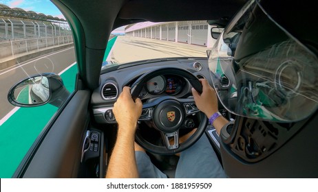 RACETRACK SLOVENIA, AUGUST 2020: CLOSE UP: Adrenaline Seeking Man Cruises In His Porsche Along The Pit Lane Of An Open Racetrack. Male Racer Drives Out Of The Pits And Towards The Closed Circuit.