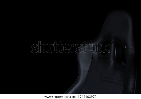 A racing\
style gaming chair sitting in darkness.\
