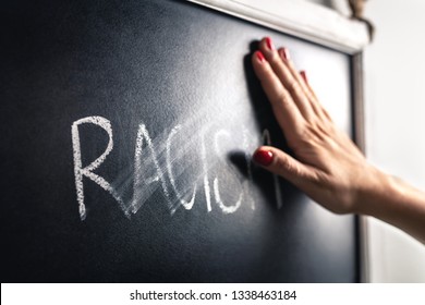 Racism Concept. Stop Hate And Discrimination. Against Prejudice And Violence. Hand Wiping Off And Erasing The Word From Blackboard.