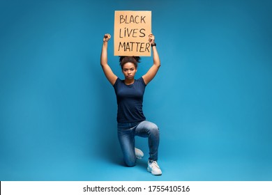 Racism discrimination strike. African american woman protesting with placard Black Lives Matter, standing on one knee, blue studio background