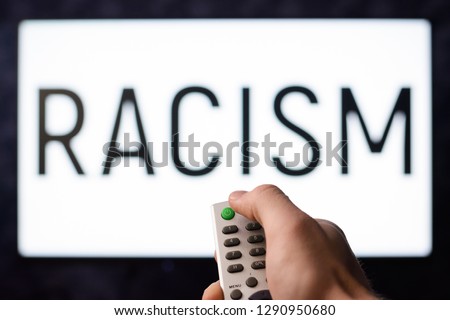 Racist male with remote controller turns on a TV set with lettering RACISM