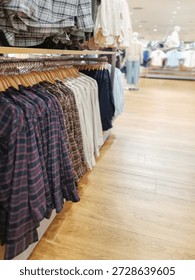 A rack of assorted plaid and solid color shirts hangs in a bright retail clothing store with wooden floors, offering a variety of fashion choices for shoppers in a modern shopping environment.