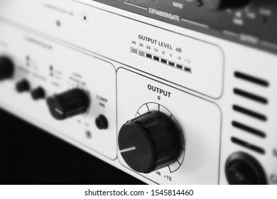 A Rack Of Audio Compressors And Other Components Of Sound Reinforcement System In A Recording Studio Close Up. Black And White Photo. Output Knob And Sound Level Control Macro