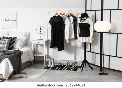 Rack with clothes and folding screen in interior of bedroom