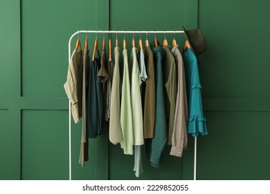 Rack with clothes and hat near green wall - Powered by Shutterstock