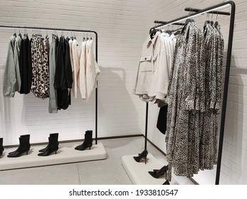 Rack With Clothes On Hangers And Shoes In The Store Against The Background Of A Small Wall