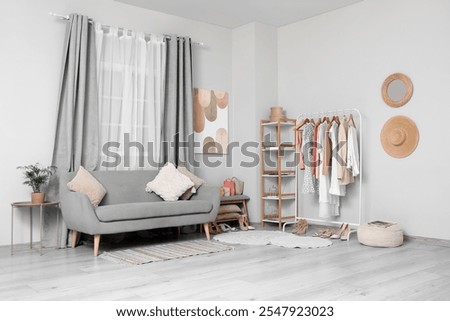 Rack with clothes and stylish sofa in interior of dressing room