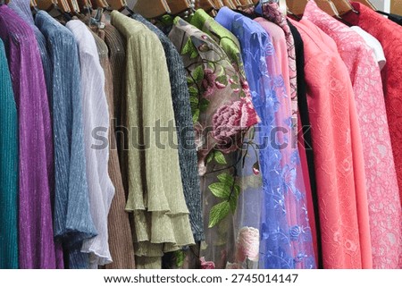 Rack of clothes with  variety of colors and patterns. clothes hanging on a rack, and  colors include blue, pink, and green