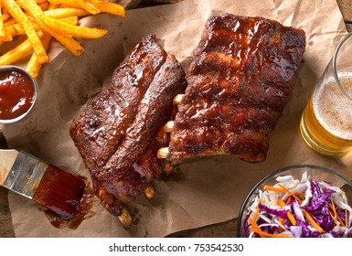 A rack of delicious baby back ribs with barbecue sauce, french fries, coleslaw and beer.