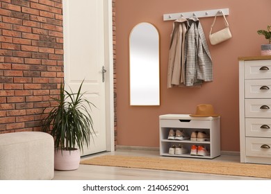 Rack With Different Shoes Near Pale Pink Wall In Hall