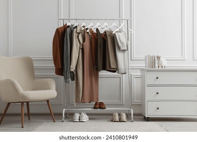 Rack with different stylish women`s clothes, shoes, dresser and armchair near white wall in room - Powered by Shutterstock