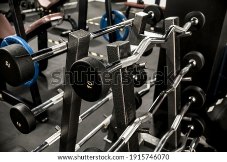 A rack of EZ and straight bar barbells with fixed weights at a gym or fitness club.
