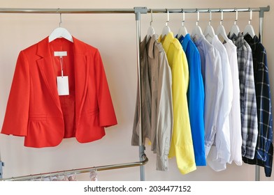 Rack with fashionable new clothes with label, bright orange suit and colorful shirts 