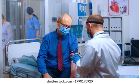 Rack Focus From The Elevator Of Busy Hospital Or Private Health Clinic, Everebody Wearing Masks. Doctor Measuring Blood Pressure, Nurse Helping Old Retired Lady. COVID-19 Theme. Medical Medicine