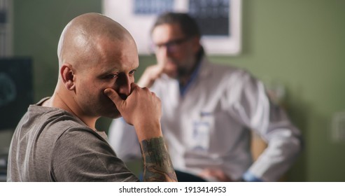 Rack Focus Of Upset Bald Male Patient With Cancer Touching Face And Crying Then Talking With Mature Doctor After Hearing Bad News