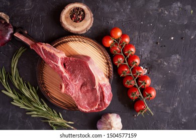     rack of lamb on a cutting board with rosemary, pepper peas, red tomatoes on a twig on a concrete dark background. BBQ cooking. Meat menu. Top view                           
