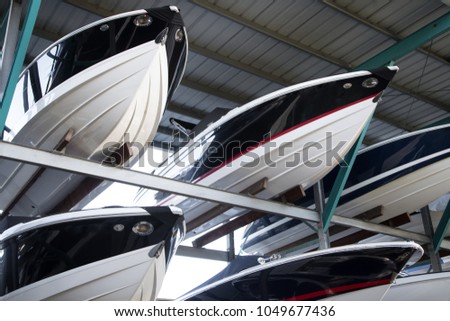  Rack of modern speedboats for sale, with pointed fiberglass hulls and bows, in a covered warehouse at a maritime storage dockyard