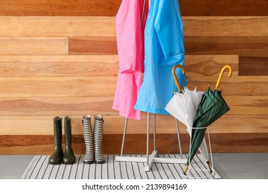 Rack with raincoats, gumboots and umbrellas near wooden wall - Powered by Shutterstock