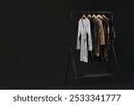 Rack with stylish dresses on black background