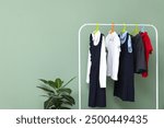 Rack with stylish school uniform and houseplant near color wall