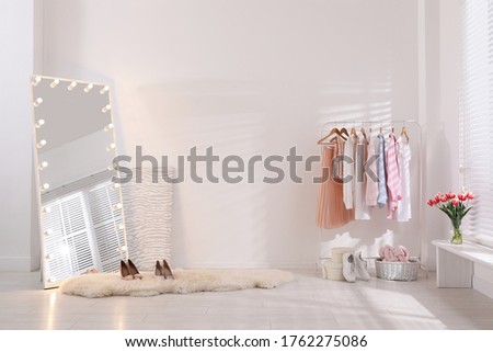 Rack with stylish women's clothes and mirror indoors. Interior design