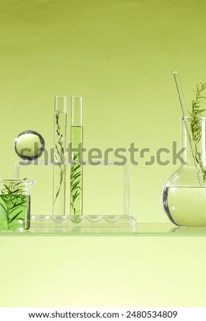 A rack of test tubes, a beaker and a flask of transparent and green liquid displayed on a glass panel. Front view. Tea tree oil may have natural benefits for topical use