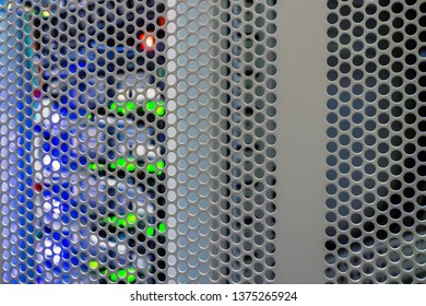 Racks with server hardware are located behind an iron door with round openings. Storage blades flashing lights are in a modern data center. Computer technological background.