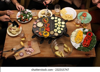 Raclette grill party - friends eating grilled vegetable, drinking beer on vintage wooden desk