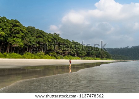 Radhanagar beach in Havelock Island, Andaman Island, India. White sand beach and blue skies. The girl walks alone on the most beautiful beach in Asia. reflection of the girl on the shiny wet sand