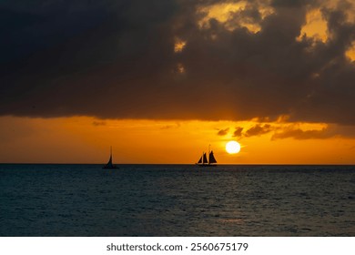 A radiant golden sunset casts shimmering light across calm waters. Silhouetted sailboats gently drift, their dark forms contrasting with the fiery hues of the sky, evoking serenity and wonder. - Powered by Shutterstock