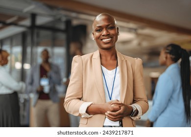 Radiant professional African American woman stands smiling confidently in a business setting, with colleagues engaging in conversation in the soft-focused background.  - Powered by Shutterstock