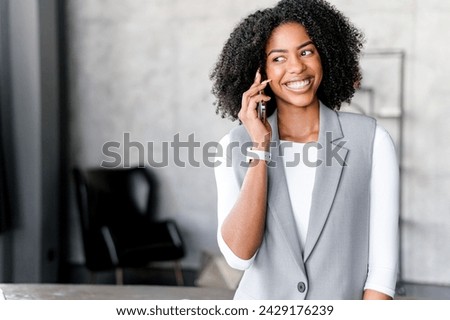 With a radiant smile, an African-American businesswoman converses on her phone, effortlessly blending professional acumen with modern connectivity in office, effective communication in the digital era
