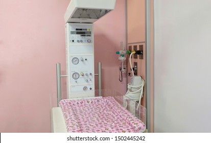 A Radiant Warmer Machine For Baby-born After Delivery For Warming, Drying And Resuscitating With Pink Bed Sheet And Oxygen Flow Meter, Oxygen Pipeline And Suction Equipment On Wall In Hospital