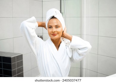 Radiant woman adjusts her towel turban in a bright bathroom setting - Powered by Shutterstock