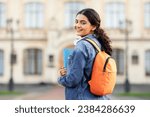 A radiant young Indian scholar with her academic books and bag, posing outside her educational institution, offering a warm smile to the lens. Space for caption, emphasizing education.