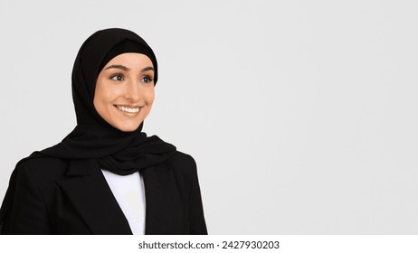 Radiant young woman wearing hijab and black blazer with beaming smile, standing against light grey background, embodying professionalism, free space - Powered by Shutterstock