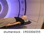 Radiation proton therapy. Brain cancer child patient lying on positioning bed with fixing mask on her head in treatment room.