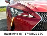 Radiator grill and headlight on a red car on a sunny day. Close-up. Horizontal orientation.