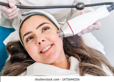 Radio frequency microneedling machine handpiece on the cheek of a woman's face during a beauty skin tightening treatment.