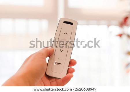 Radio remote control panel for blinds and roller shades in woman hand, white, close-up. Bright background. Blinds and curtains for smart house. Home automation, wireless technology. Electronic device.