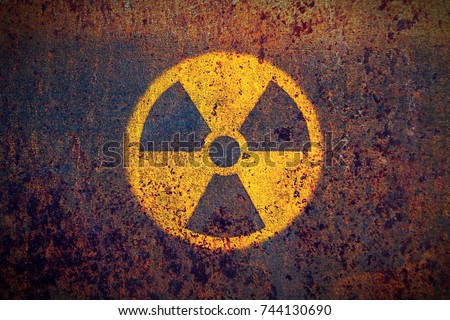 Radioactive (ionizing radiation) round yellow and black danger symbol painted on a massive rusty metal wall with dark rustic grunge texture background. Nuclear, radioactive alert concept.