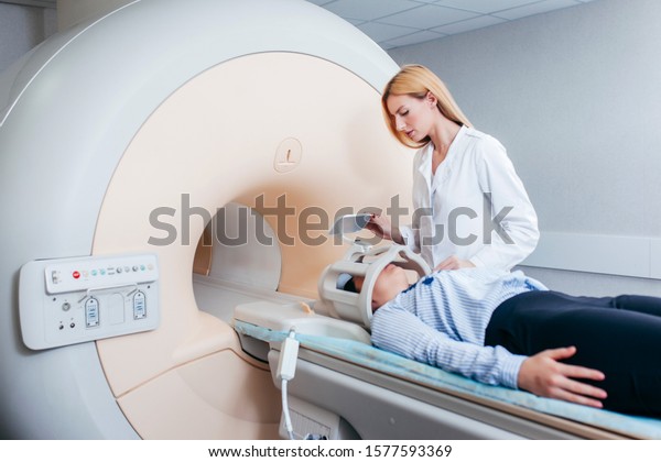 Radiologic blonde model technician help at\
mature female patient lying on a CT Scan\
bed