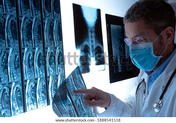 Radiologist doctor\
with face mask examining spinal column by radiography, x-ray and\
magnetic resonance imaging scan in hospital. Medical check-up and\
diagnosis. Health care\
concept.
