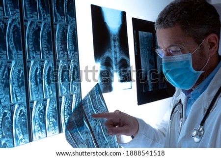 Radiologist doctor with mask examining spinal column by radiography, x-ray and magnetic resonance imaging scan in hospital. Radiology medical diagnostic. Health care and health insurance concept.