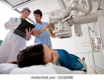Radiologist with male technician looking at clipboard while setting up the machine to x-ray female patient